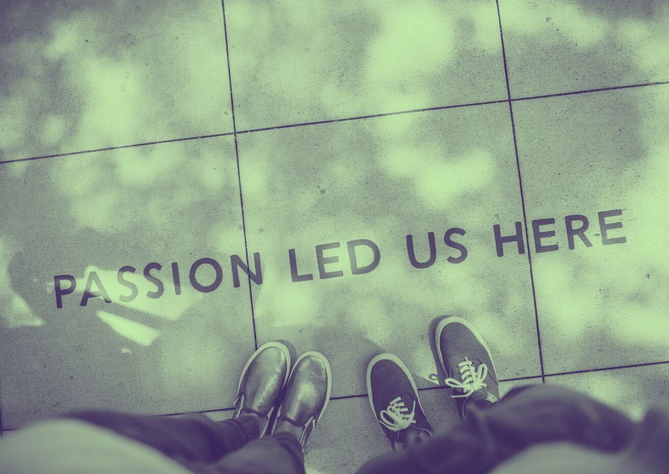 Two pairs of feet on a pavement in front of a sign that says passion led us here