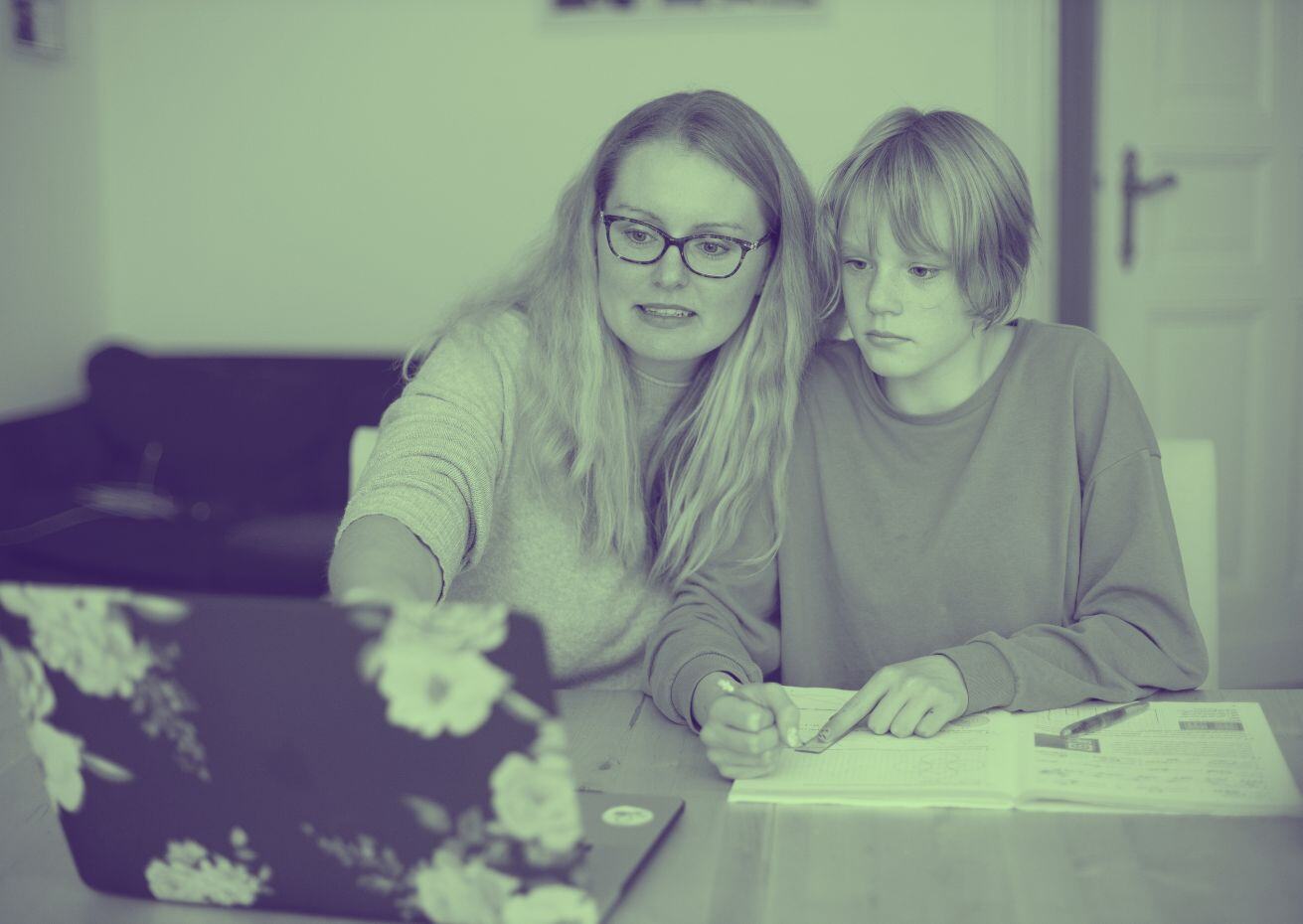 A tutor supports a child as they look at a laptop and a textbook